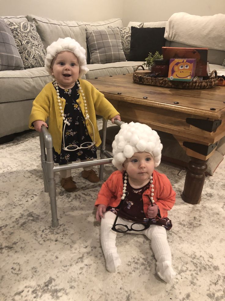 two small children sitting on the floor in front of a table and couch, wearing wigs