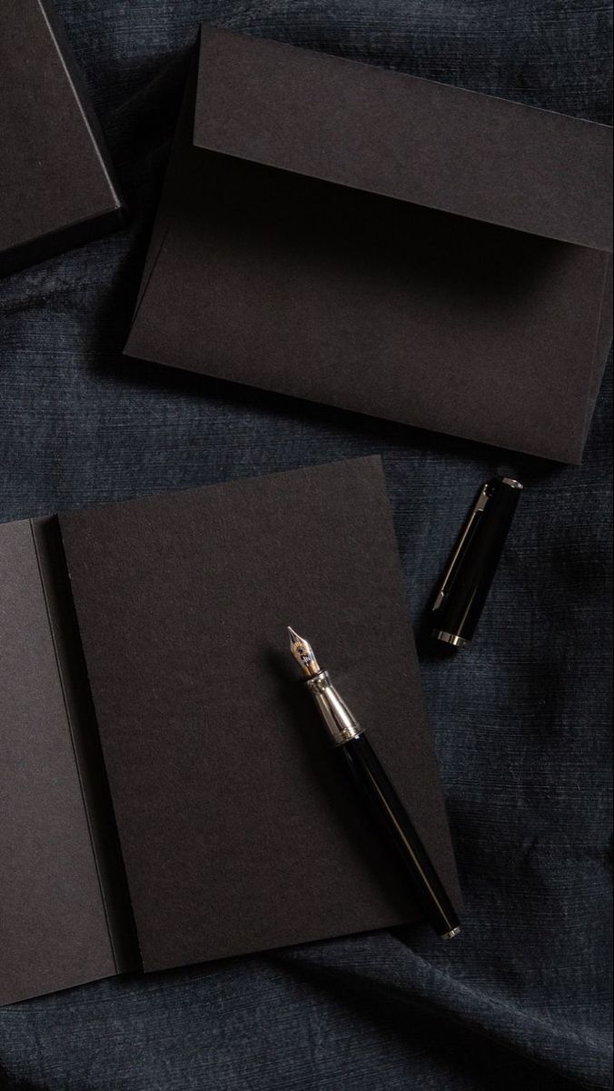 two black notebooks and a pen on a blue cloth