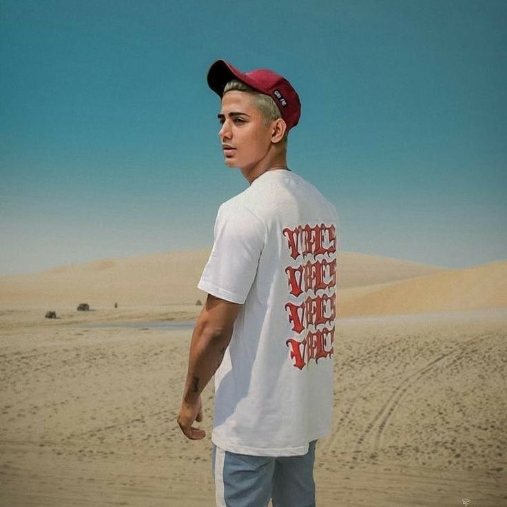 a young man standing in the desert wearing a red hat and white t - shirt