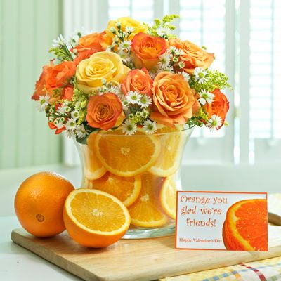 an arrangement of oranges and roses in a vase on a table with a card