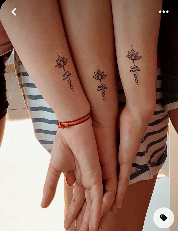 two women holding hands with tattoos on their arms and fingers, both showing the same tattoo design