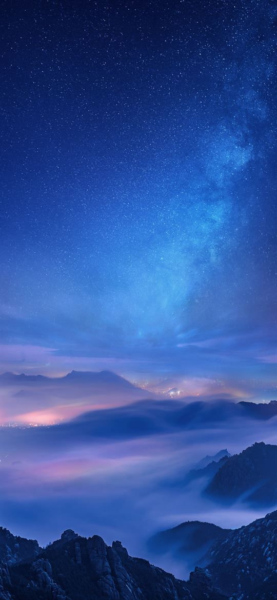 the night sky is full of stars and clouds above mountains with low lying fog in the foreground