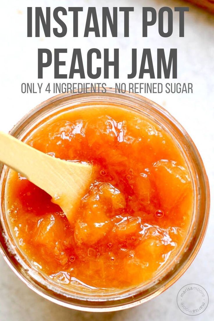 a jar filled with peach jam on top of a white table next to a wooden spoon