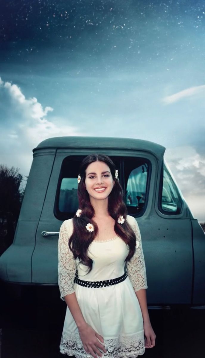 a woman standing in front of a green truck with flowers on her hair and wearing a white dress