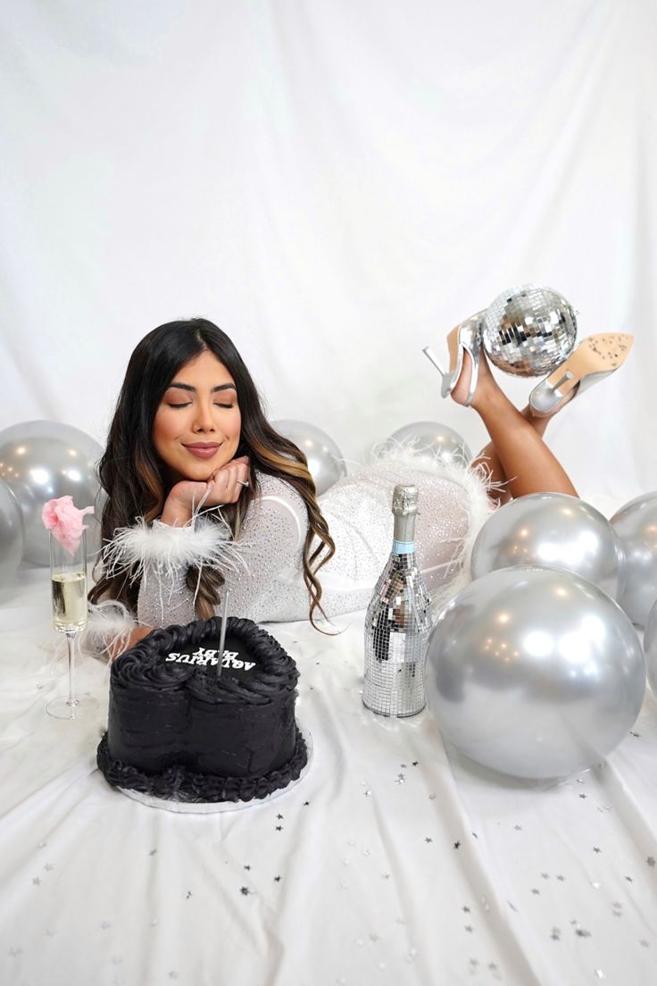 a woman sitting at a table with silver balloons and a cake in front of her