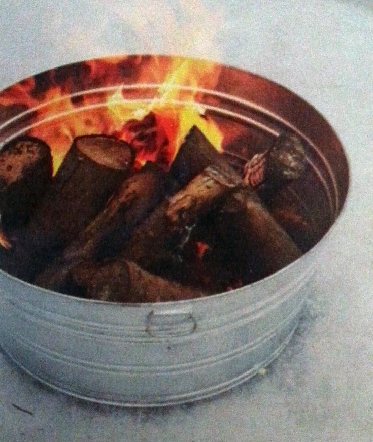 a metal container filled with fire logs on top of a cement floor next to a brick wall