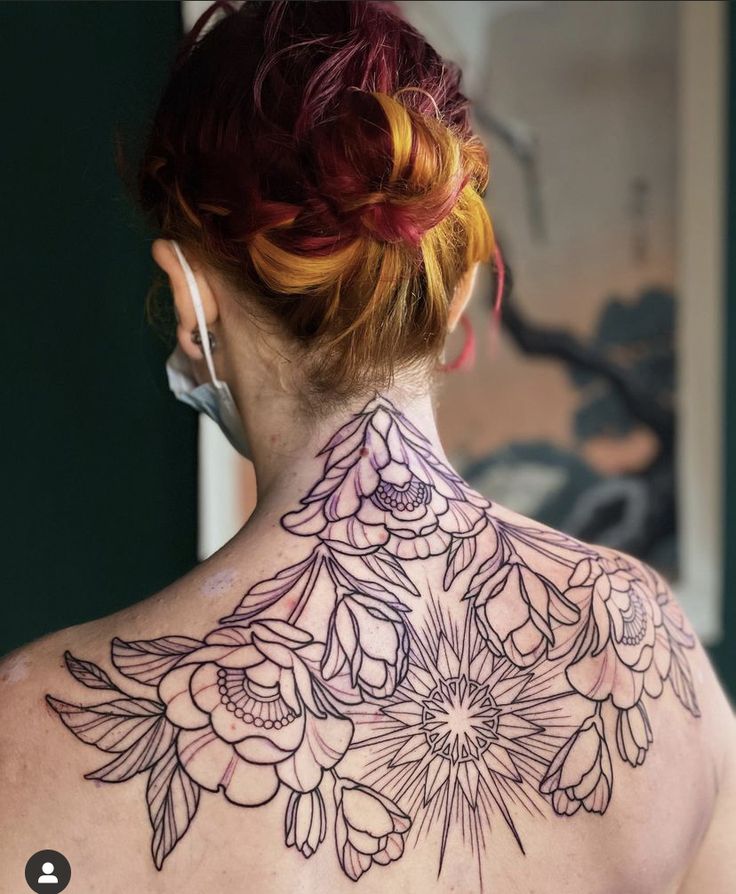 the back of a woman's neck with flowers tattooed on her upper and lower part