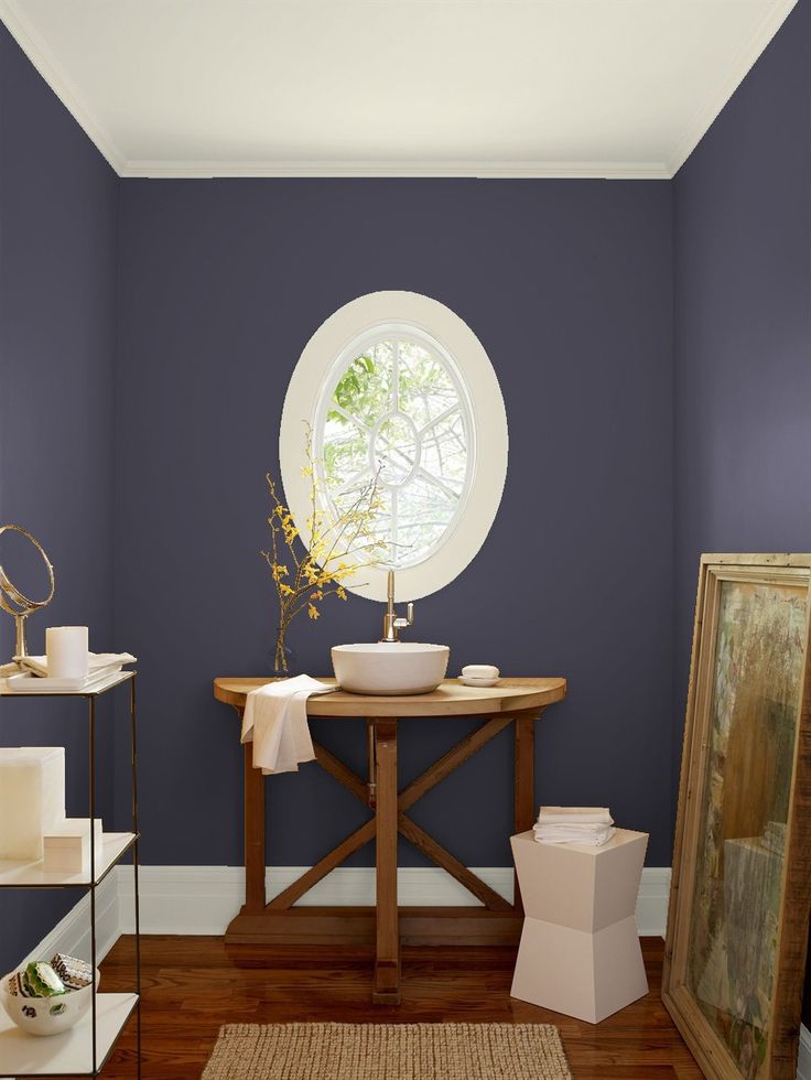 a bathroom with blue walls and wood flooring is pictured in this image, there is a round window on the far wall