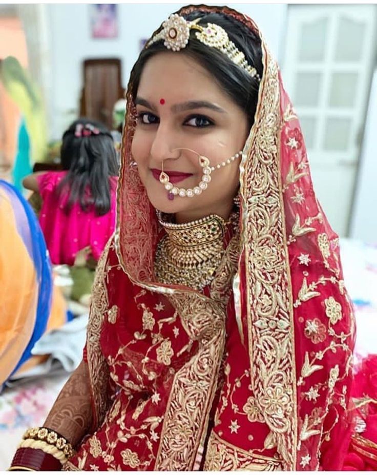 a woman in a red and gold bridal outfit with jewelry on her head, posing for the camera