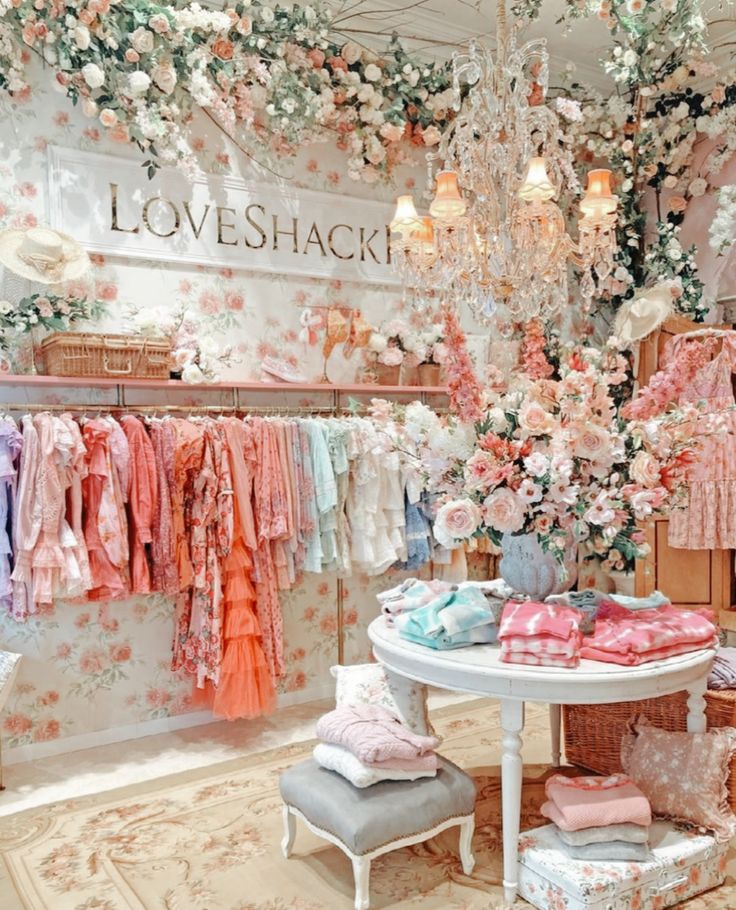 a room filled with lots of pink and white clothes hanging from the ceiling next to a chandelier