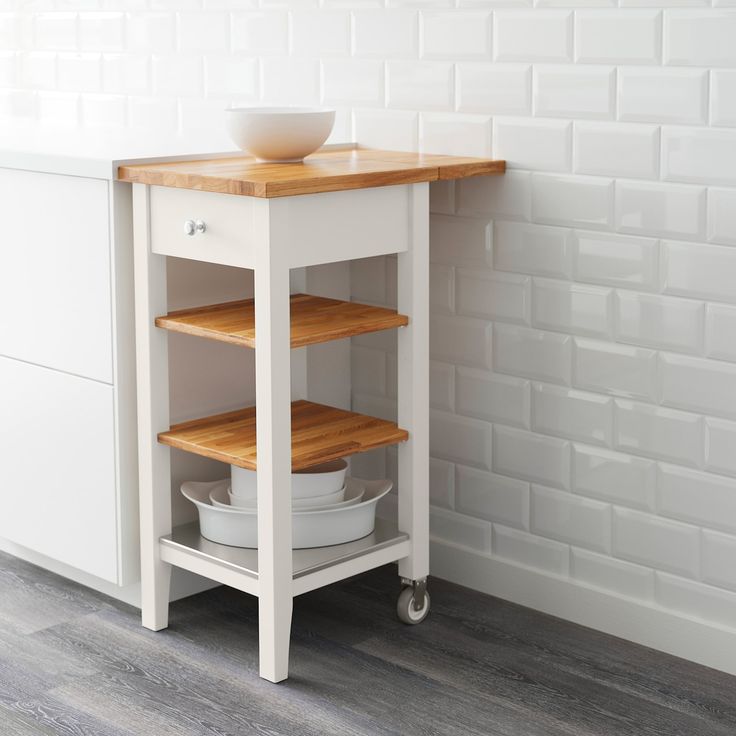 a white kitchen island with two shelves and a bowl on the bottom shelf next to it