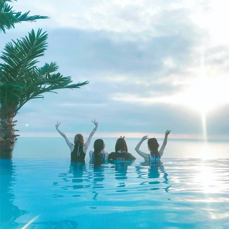 three women in the pool waving at the sun