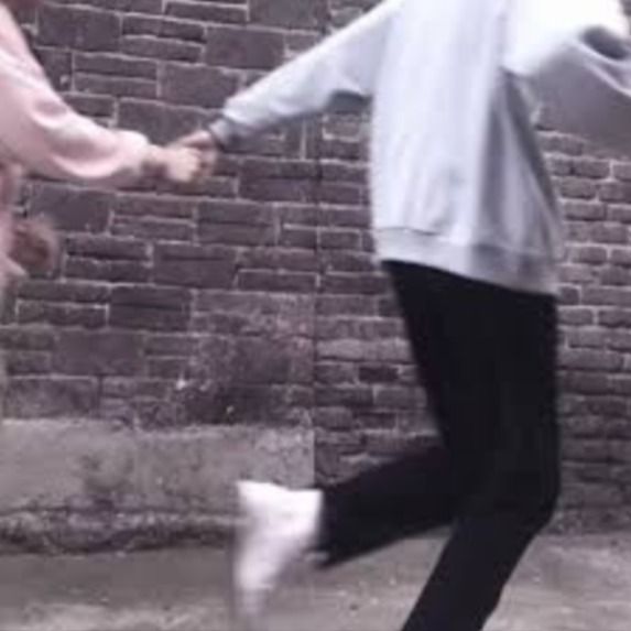 two people holding hands in front of a brick wall and one person jumping up into the air