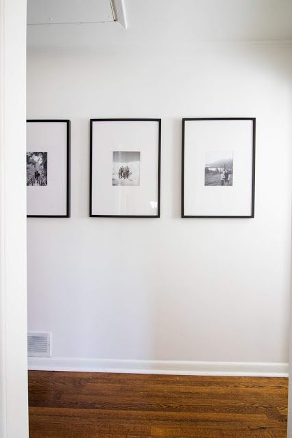 three black and white pictures hang on the wall next to a wooden floor in an empty room