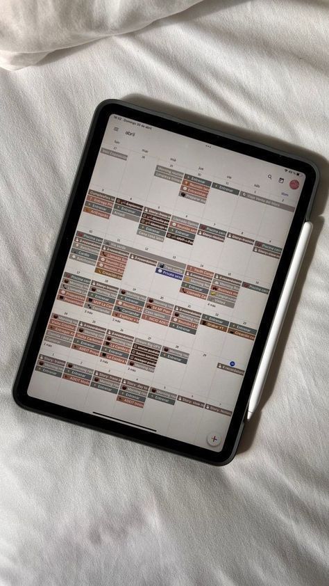 a tablet computer sitting on top of a white bed covered in sheets and pillows, next to a pen