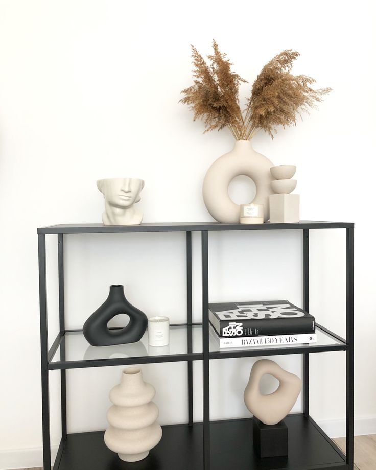 a black shelf with vases and books on it in front of a white wall