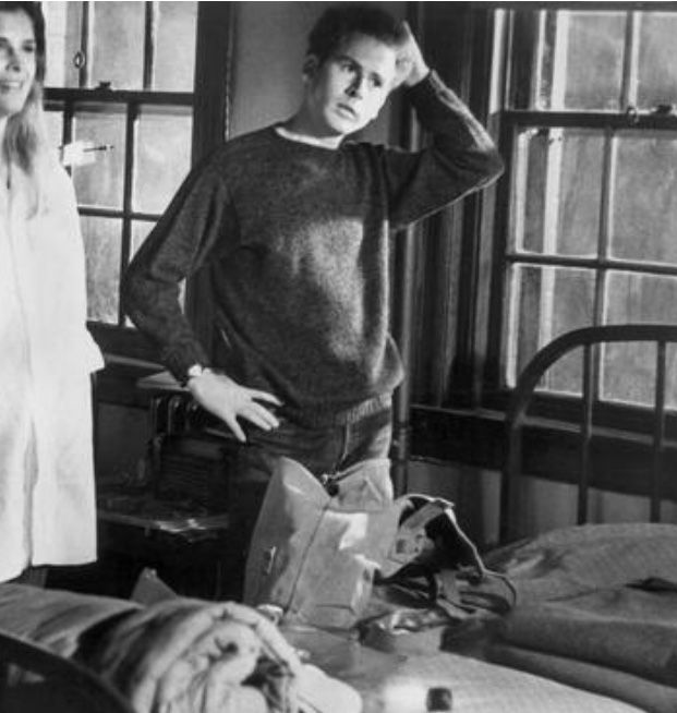 black and white photograph of two women standing next to a bed in a hospital room