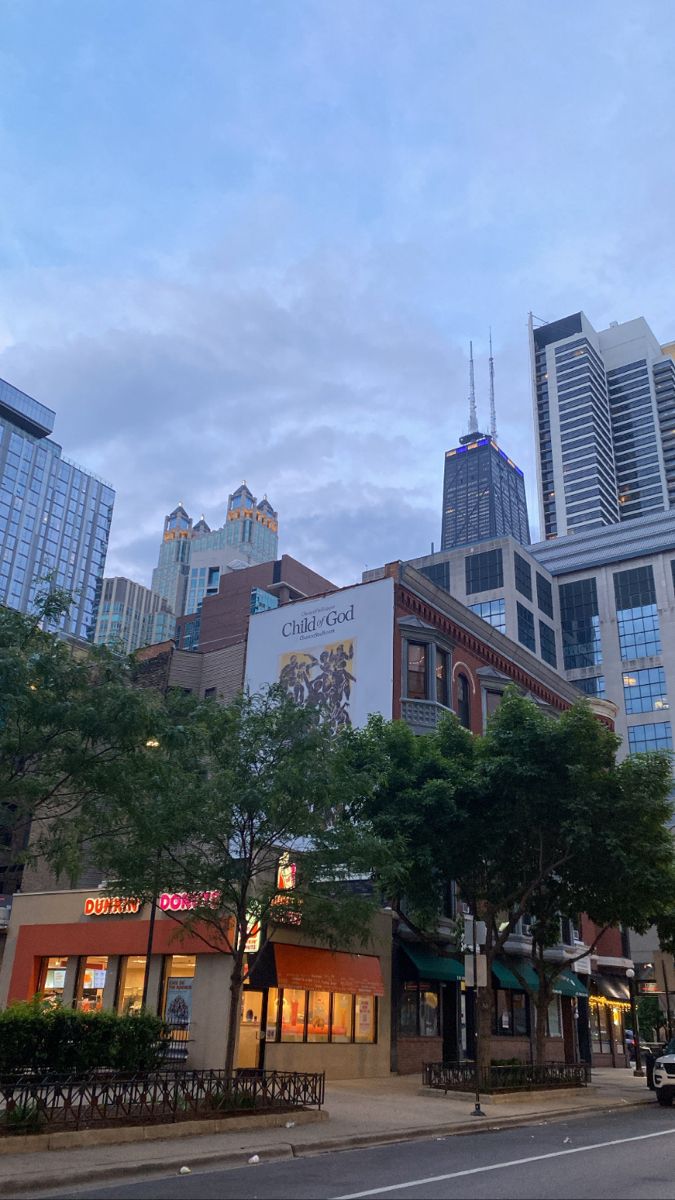 a city street with tall buildings in the distance and trees on either side of the road