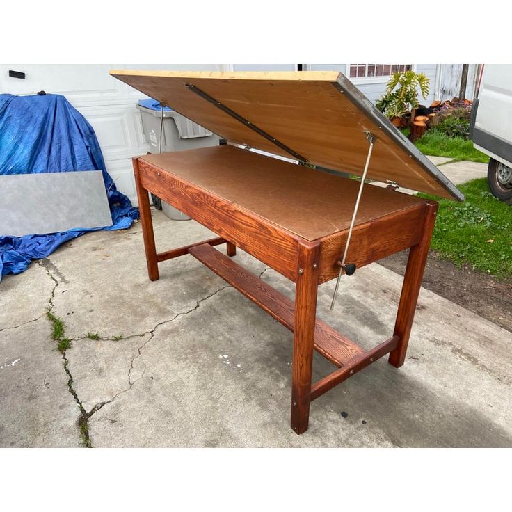 a wooden table with an open top sitting in front of a blue tarp on the ground