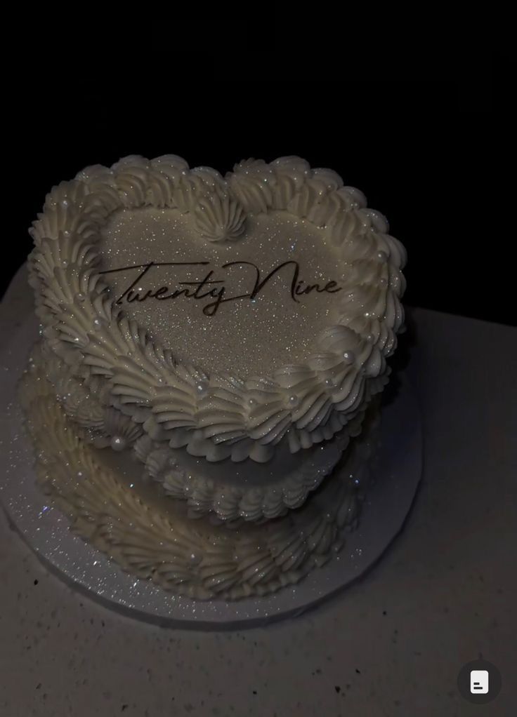 a heart shaped cake with frosting and writing on the top is sitting on a table