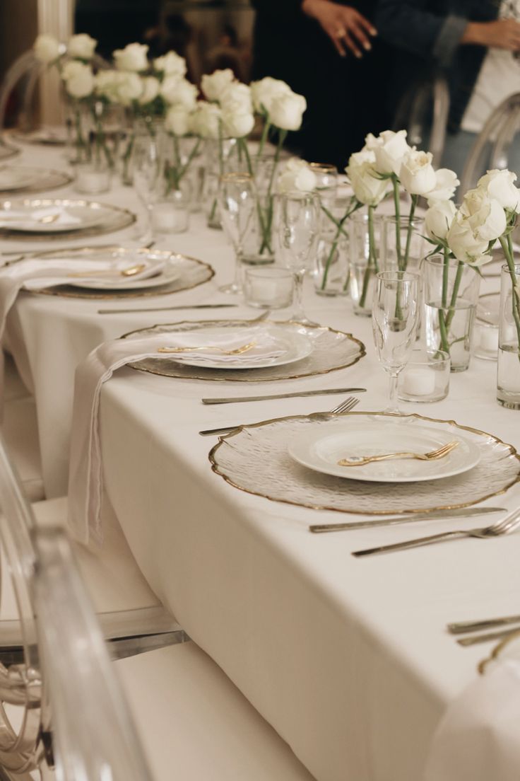 the table is set with white flowers in vases and place settings for dinner guests