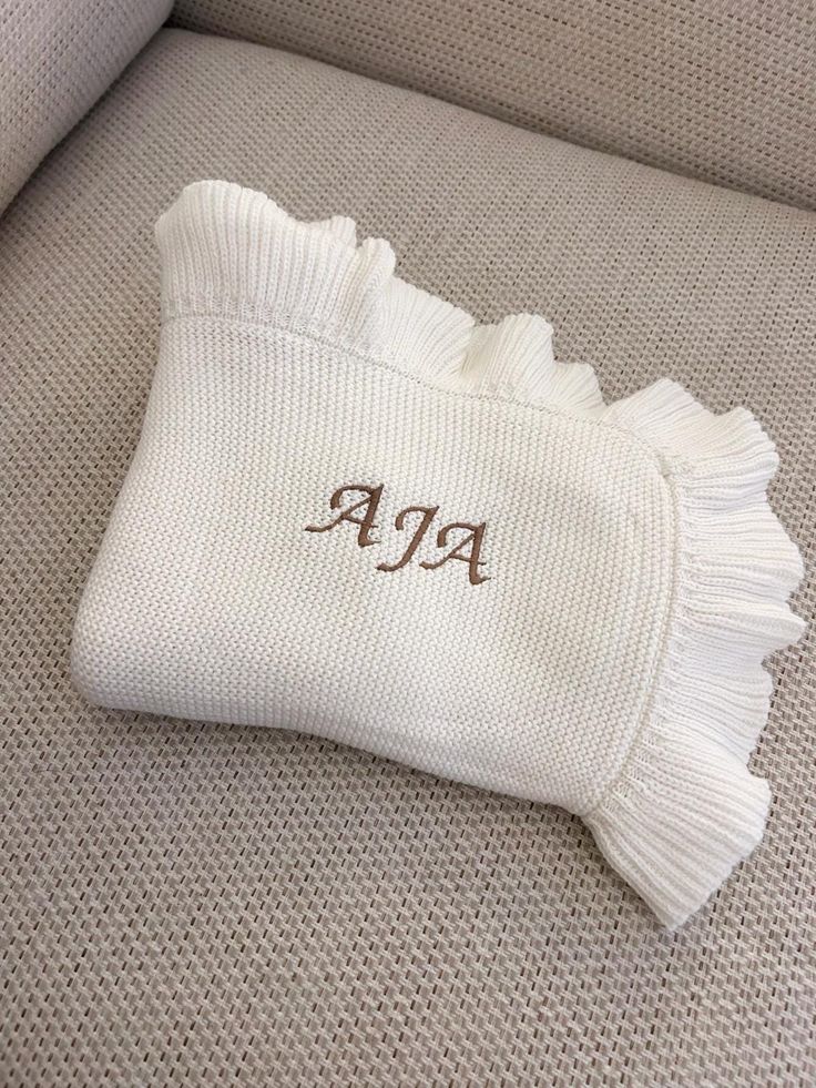 a white sweater laying on top of a couch next to a pillow with the word ap written on it