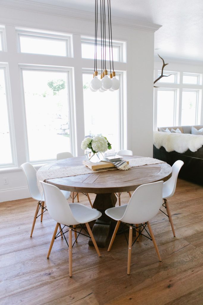 a dining room table with white chairs in front of large windows and wooden flooring