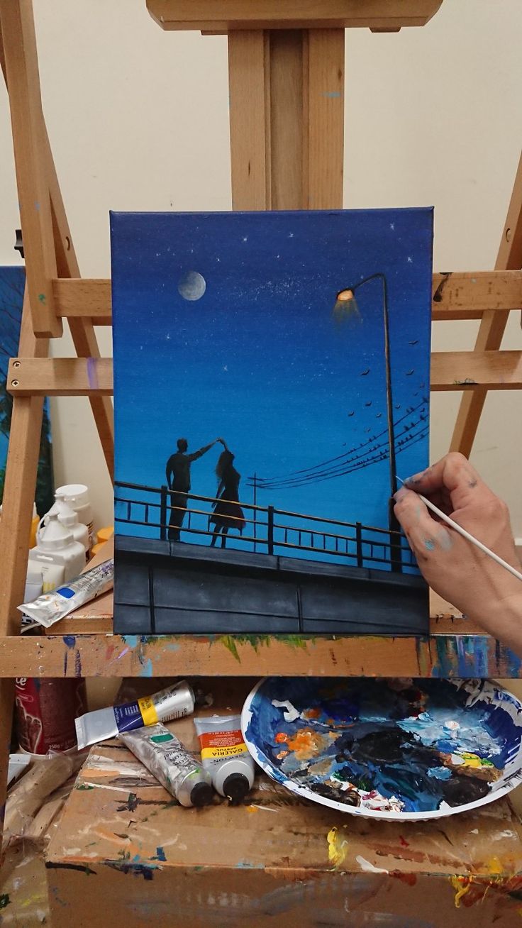 a person is painting on an easel in front of a blue sky with the moon