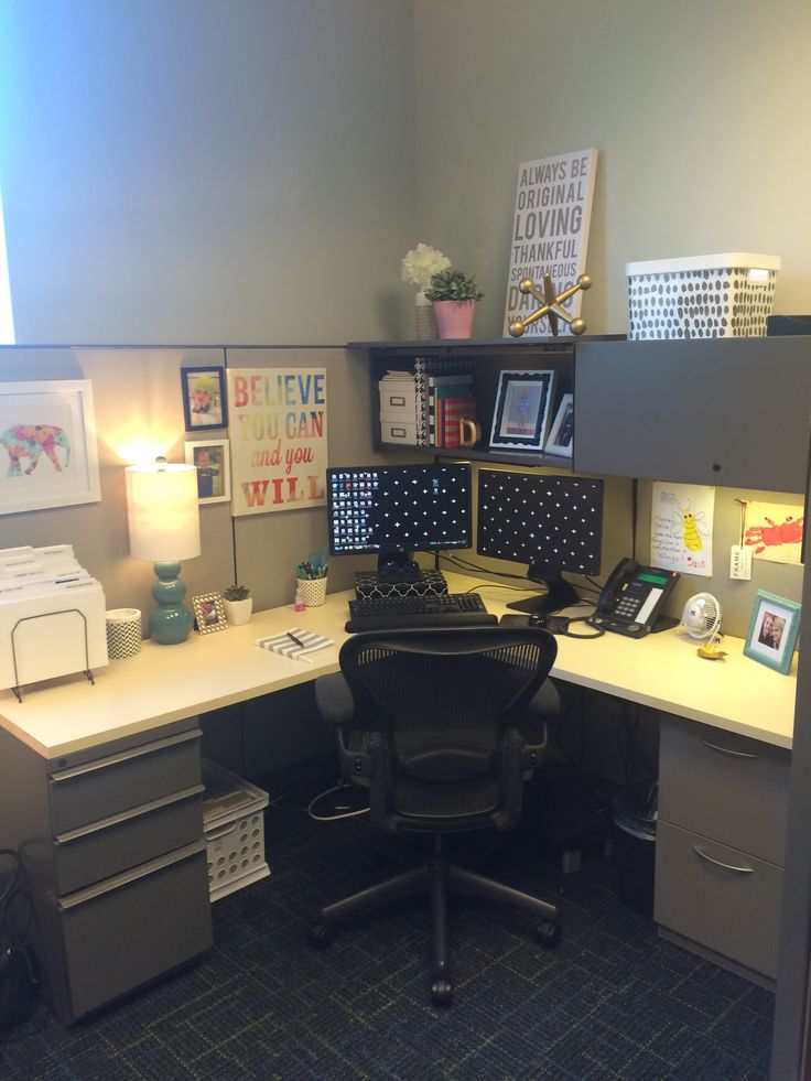 an office cubicle with two computer desks and file cabinets on each side, in front of a gray wall