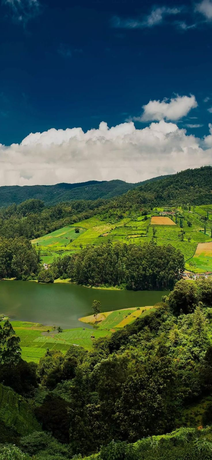 a lake surrounded by lush green hills under a blue sky with white clouds in the distance