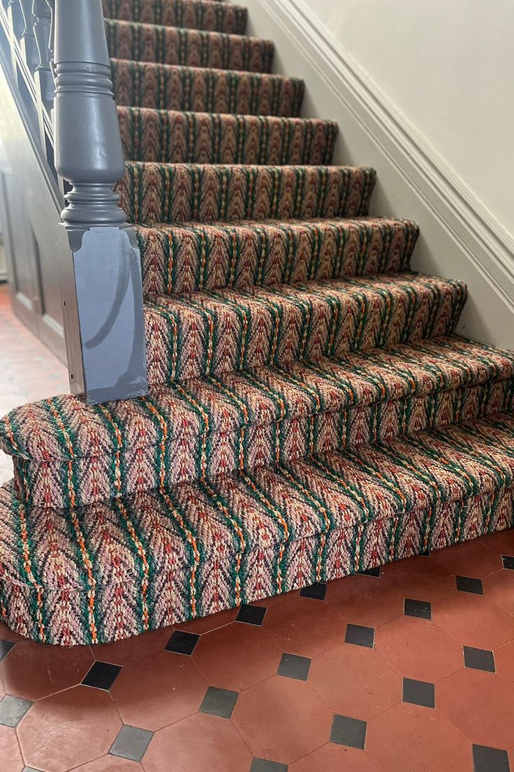 a carpeted stair case next to a hand rail on a tiled flooring area