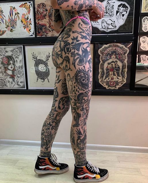 a woman with tattoos standing in front of a wall full of tattoo designs on her body