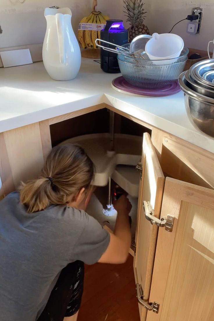 a woman is working in the kitchen under the sink and looking for something to eat