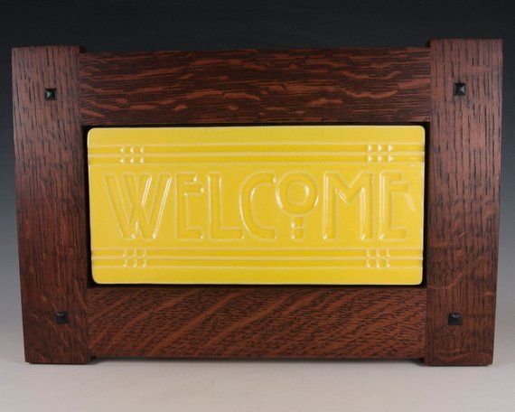 a yellow welcome sign in a wooden frame on a gray background with the word welcome