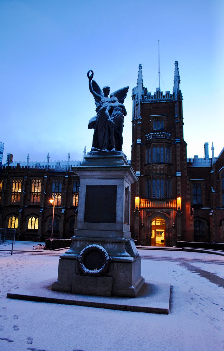 a statue in front of a building with snow on the ground and lights behind it