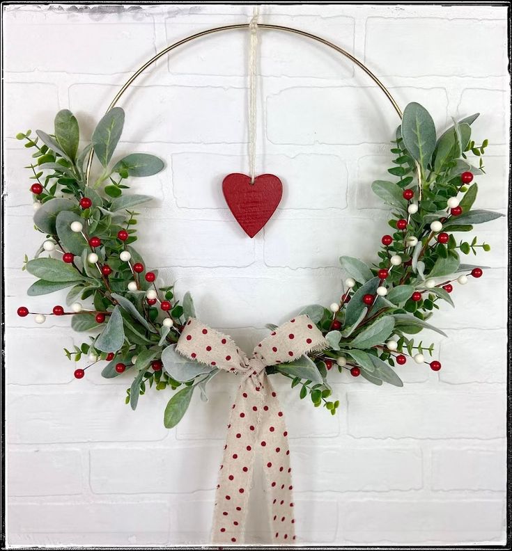 a christmas wreath hanging on a wall with a red heart in the middle and greenery around it