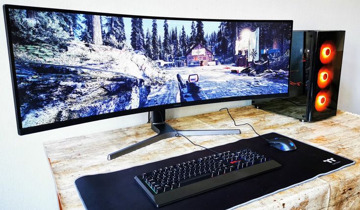 a computer monitor and keyboard sitting on top of a wooden desk in front of a large screen