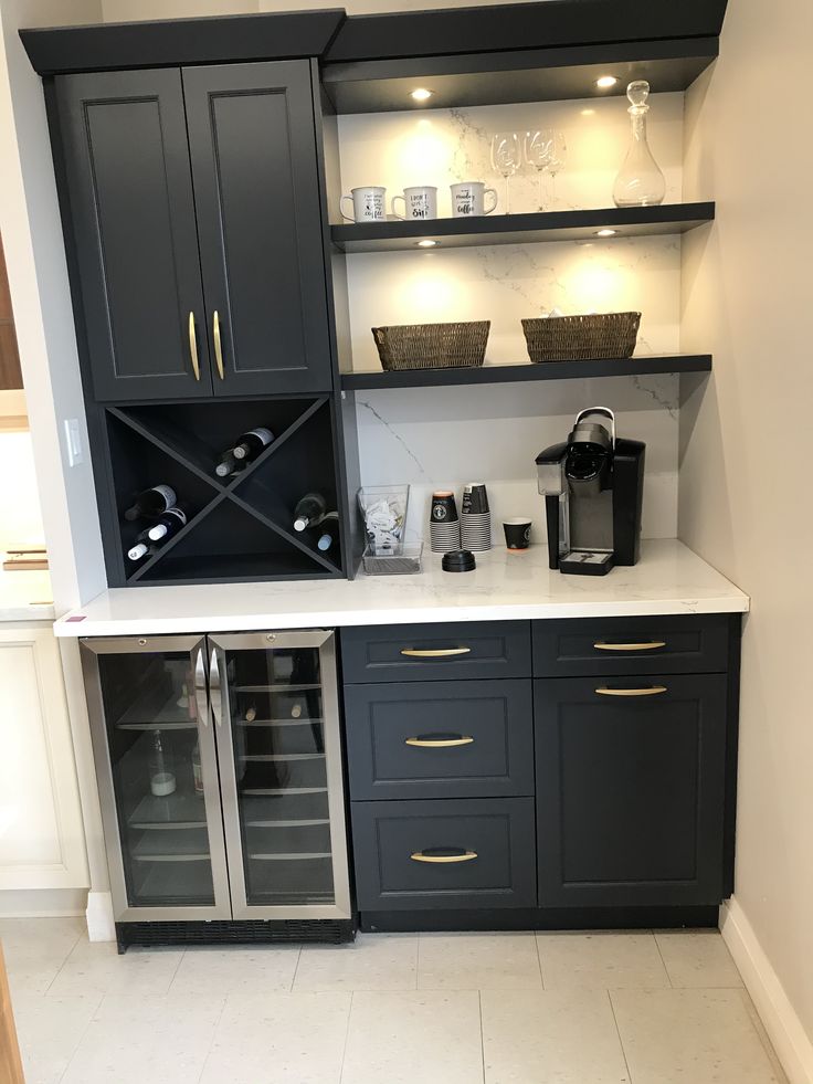 a kitchen with black cabinets and white counter tops, wine glasses on the shelves in front of it