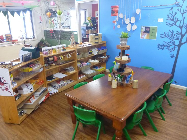 a room filled with lots of wooden tables and green chairs next to shelves full of books