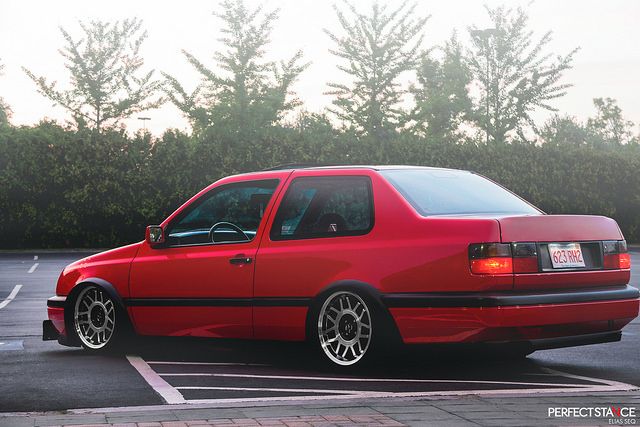 a red car parked in a parking lot with trees in the background