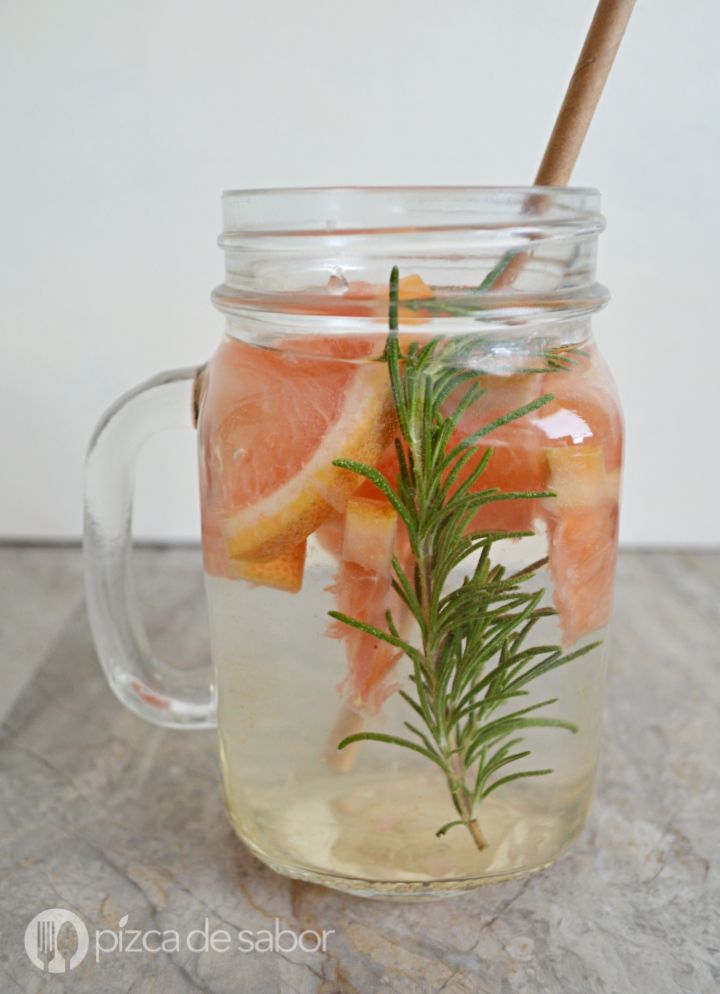 a mason jar filled with water, orange slices and rosemary sprig on top