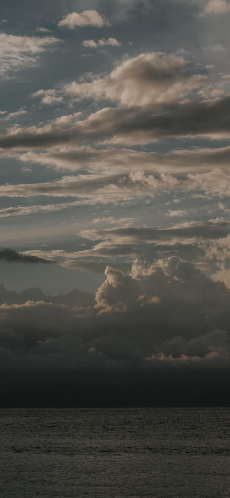 an airplane flying over the ocean under a cloudy sky