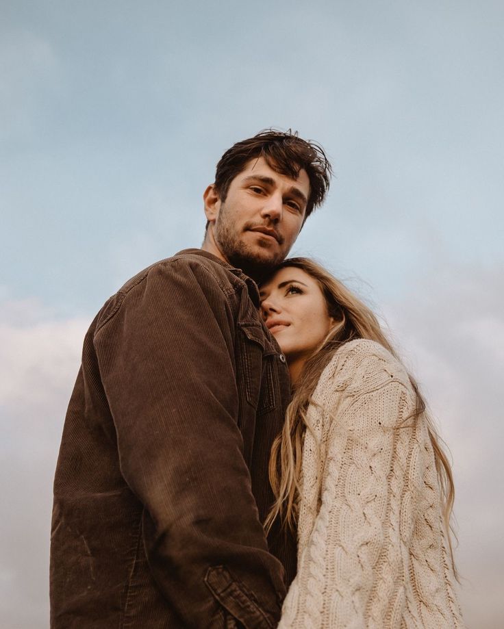 a man and woman standing next to each other in front of a cloudy blue sky