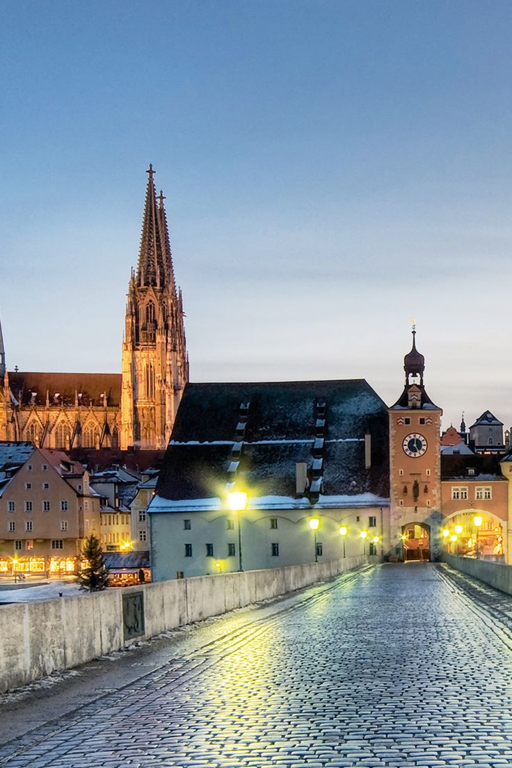 a cobblestone road leading to a cathedral in the background at night with lights on