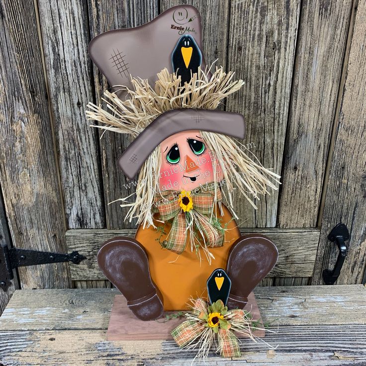 a scarecrow sitting in front of a wooden fence with hay and sunflowers