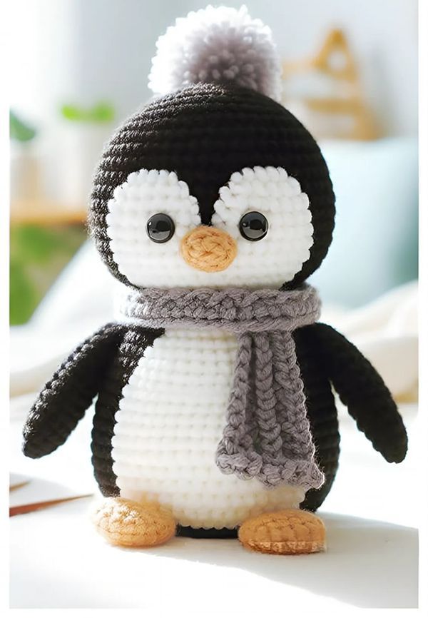 a crocheted penguin with a scarf and hat on it's head sitting on a table