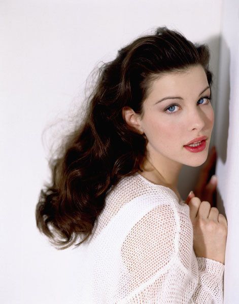 a woman with long hair leaning against a wall