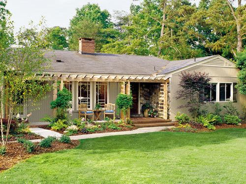 a house that is in the middle of some grass and bushes with trees around it