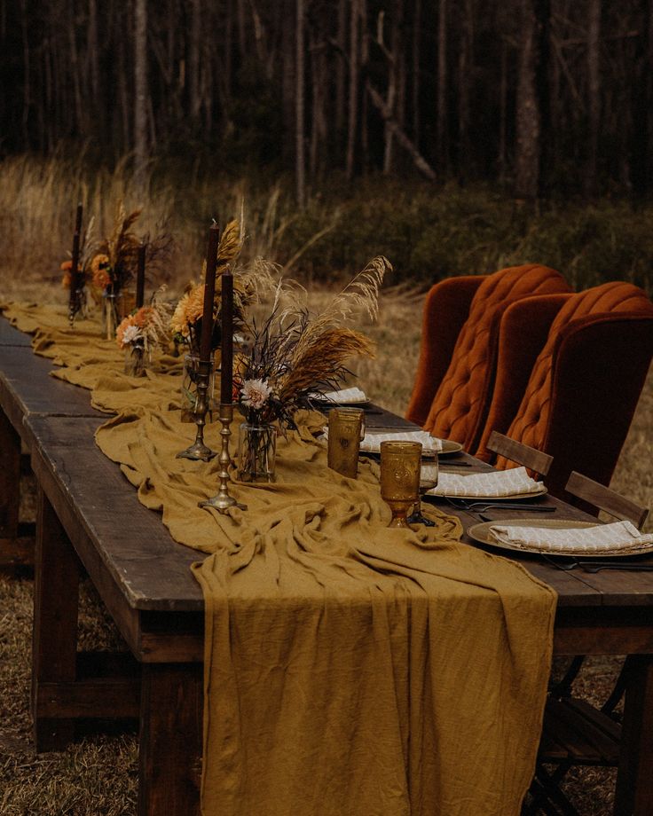 a long table set up with place settings and candles for an outdoor dinner party in the woods