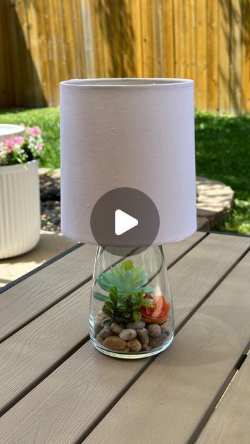 a lamp that is sitting on top of a table with rocks and plants in it